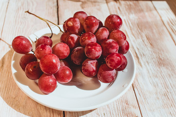 Fresh red grapes in a plate on wooden table, flatlay