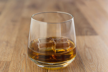 Glass of whiskey with ice on wooden background