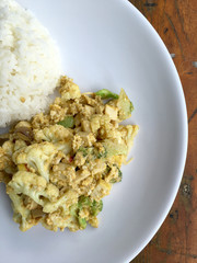 Fried cauliflower with tofu and egg in white pate on wooden table.