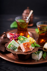 Bowl with various pieces of turkish delight lokum and black tea with mint on a dark background