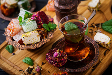 Bowl with various pieces of turkish delight lokum and black tea with mint on a dark background