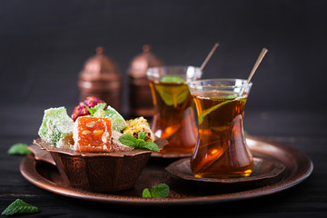 Bowl with various pieces of turkish delight lokum and black tea with mint on a dark background