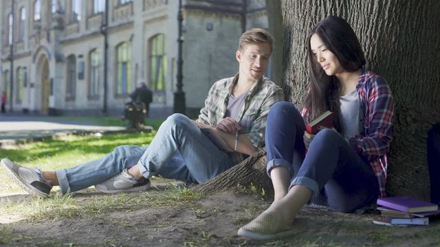 Multiracial male and female students talking under tree, acquaintance, flirting