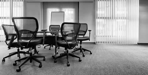 Ergonomic office chairs around a small conference table. Black and white with copy space. Banner format