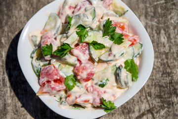Fresh salad with tomato, cucumber, onion, parsley and mayonnaise on rustic wooden table
