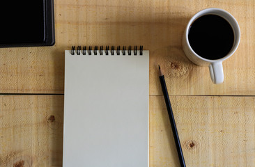 Notebook with pencil and blank white ceramic cup on wooden table