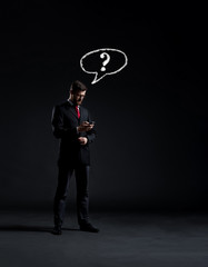 Businessman checking his smartphone over dark dramatic background. Business, office, idea concept.