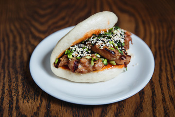 Asian gua bao with grilled chicken, teriyaki sauce, green onion and sesame seeds. Selective focus, small depth of field.
