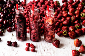detox water in three bottles with berries on white wooden background