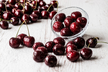 Close up of fresh cherry berries with water drops on white wooden background