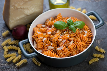 Italian fusilli pasta with red onion sauce and parmesan and its cooking ingredients, studio shot