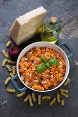 Fusilli pasta with red onion sauce and parmesan cheese over brown stone background, high angle view