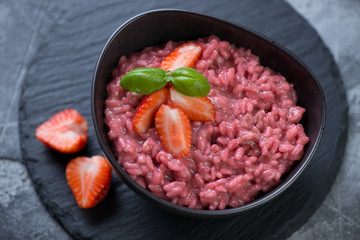 Risotto with strawberries served in a black bowl on a stone slate tray, close-up, elevated view