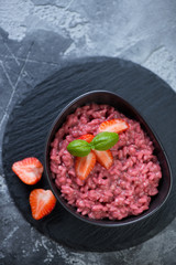 Bowl with strawberry risotto on a stone slate tray, flat-lay on a grey stone surface, vertical shot