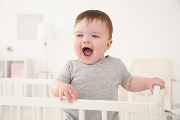 Cute little baby standing in crib at home