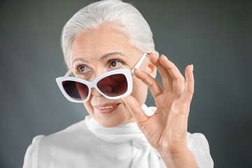 Beautiful elegant elderly woman with sunglasses on gray background