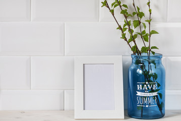 photo frame and blue glass jar with young green branches on a white background