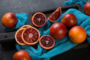 Whole and sliced sicilian blood oranges on a black wooden serving board, horizontal shot