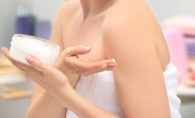 Obraz na płótnie Canvas Young woman with jar of moisturizing cream in bathroom, closeup