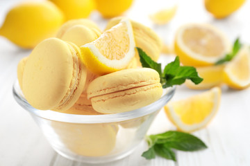 Glass bowl with tasty lemon macarons on white wooden table, closeup