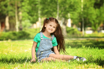 Naklejka na ściany i meble Cute little girl sitting on green grass in park