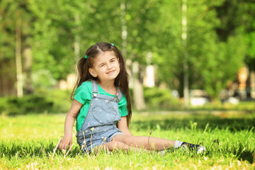 Cute little girl sitting on green grass in park