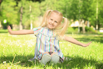 Cute little girl sitting on green grass in park