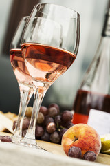 Two glasses of rose wine and board with fruits, bread and cheese on wooden table 