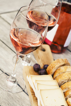 Two glasses of rose wine and board with fruits, bread and cheese on wooden table 