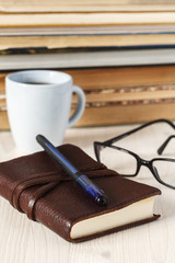 leather notebook with pen, glasses and coffee on a background of books