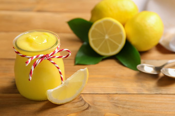 Glass jar with yummy lemon curd on wooden table