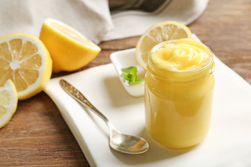 Glass jar with yummy lemon curd on wooden table