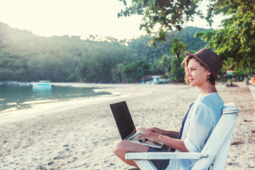 Young beautiful woman hipster traveler freelancer with laptop on the seashore. Business and vacation concept - obrazy, fototapety, plakaty