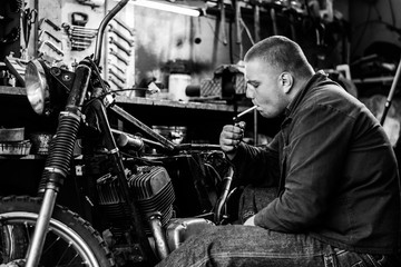 Fototapeta na wymiar Man smoke during a break of repairing old motorcycle in workshop