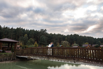 Obraz premium loving wedding couple kissing on the bridge near lake. Wedding couple in love on wedding day