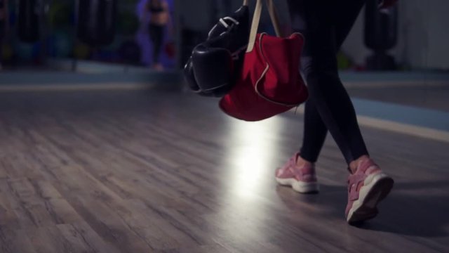 Closeup view of legs of young fit woman entering a fitness club with a bag and boxing gloves and preparing for the training in a boxing club.