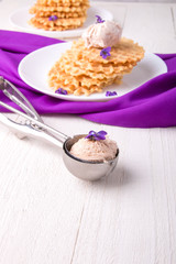 Spoon with ice cream. Belgian waffle on white plate decorated with purple flower.