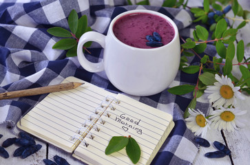Cup of smoothie with honeysuckle berries, open diary, pencil and daisy flowers on checked napkin