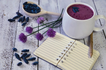 Cup of smoothie with honeysuckle berries, summer flowers and open diary with copy space 