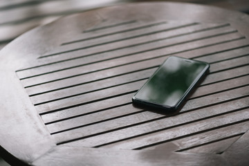 smartphone placed on the wooden table at the coffee shop in selective focus. Concept : forget,...