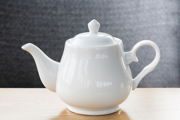white ceramic kettle on the wooden table in selective focus.