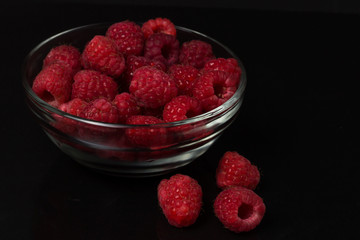 Raspberries in a glass bowl on a black background