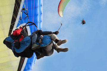 Two paraglider tandem fly against the blue sky,tandem paragliding guided by a pilot - obrazy, fototapety, plakaty