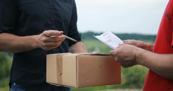 Man hands accepting a delivery of boxes from deliveryman, countryside field background courier
