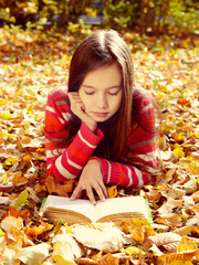 girl lying on fallen leaves and reading a book