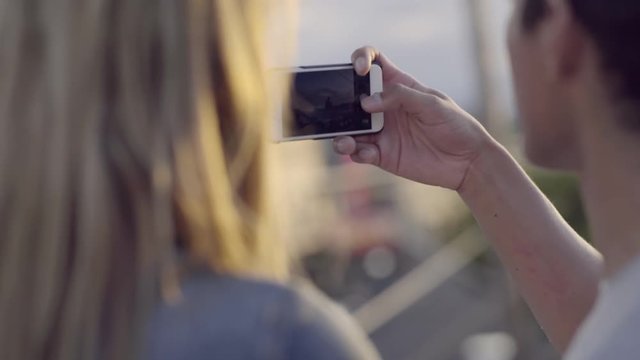 Cute Young Couple Watch Sunset Over City From Rooftop, Man Takes Panorama Photos On Phone 
