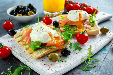 Poached egg on grilled toast with smoked salmon, rucola, olives, vegetables and orange juice. on white board. healthy breakfast