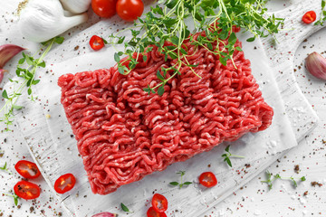 Fresh Raw Beef Minced Meat with salt, pepper, chilli and fresh thyme on white board.