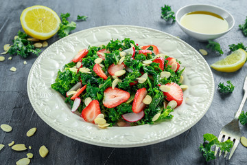 Healthy kale salad with strawberries and almond in a white plate