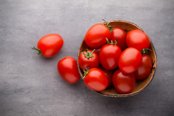 Small plum tomatoes in a wooden bowl on a gray background.